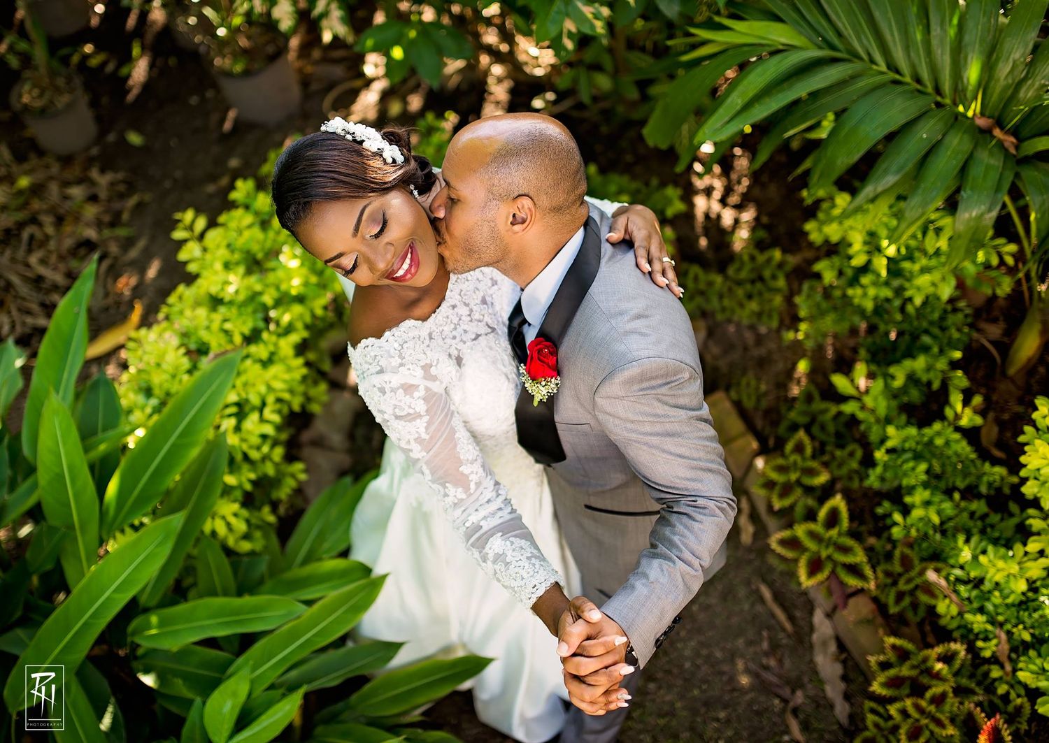 Wedding couple shares joyful moment among tropical garden foliage.