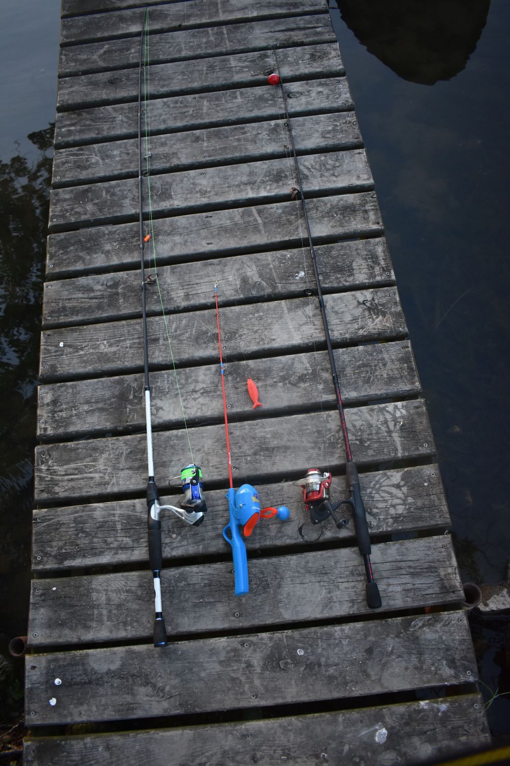 Fishing poles and tackle rest on a wooden dock over dark water.