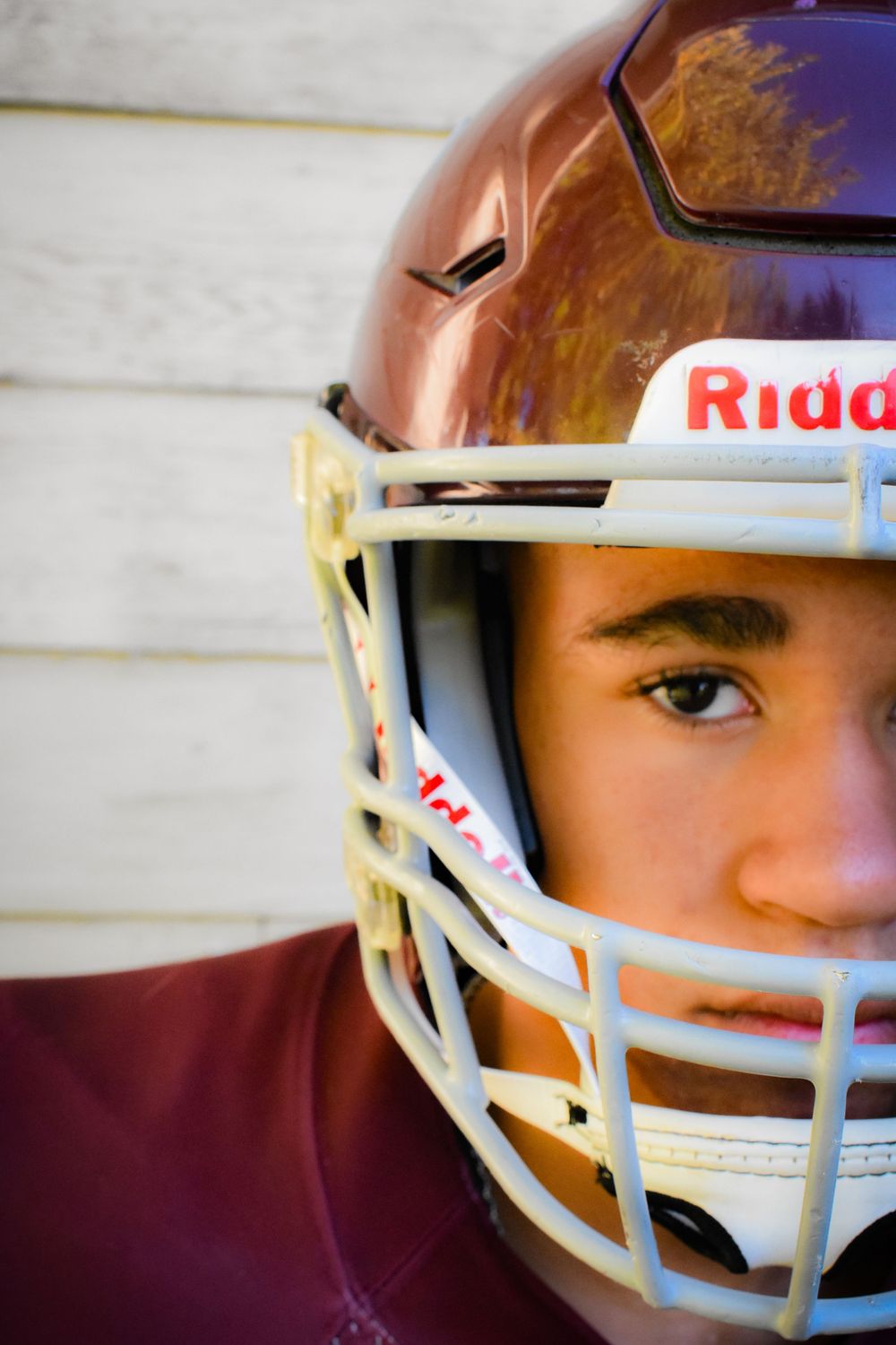 Close-up of football player wearing copper and white Riddell helmet.