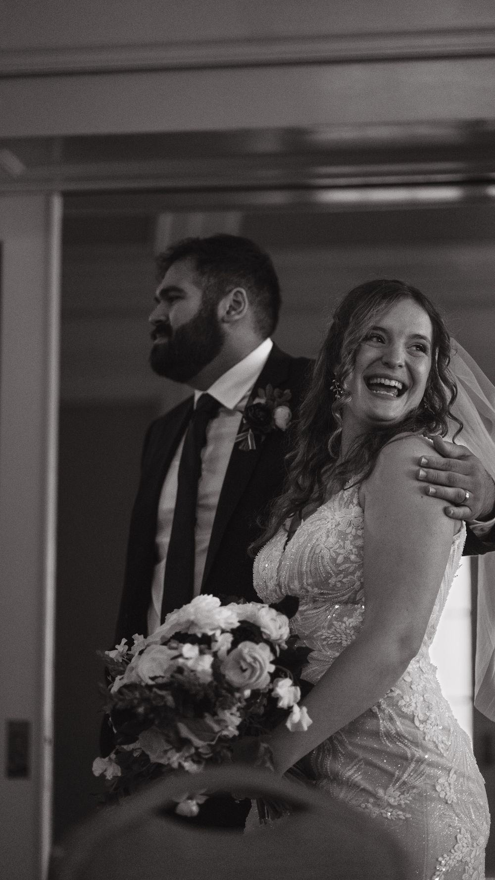 A joyful wedding moment captured in black and white showing a couple with the bride holding a floral bouquet.