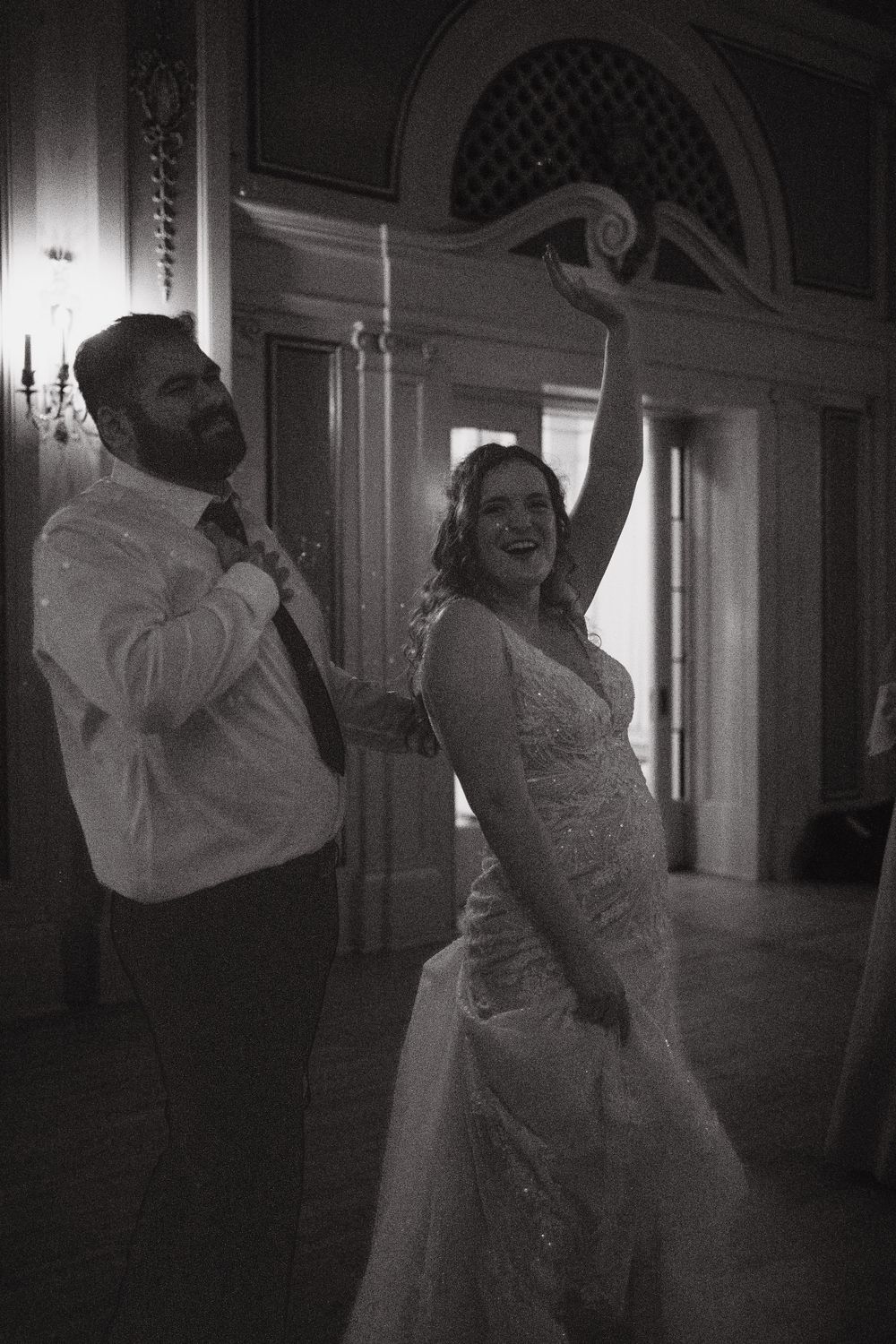 Black and white photo of newlyweds dancing together in an elegant venue with ornate architectural details.