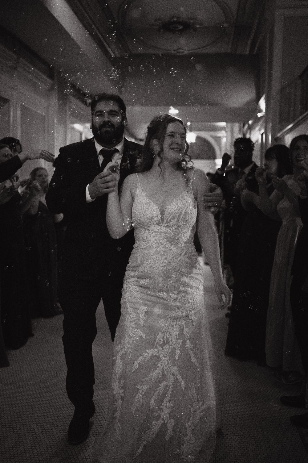 Couple celebrating at their wedding reception while walking through a hallway filled with guests.