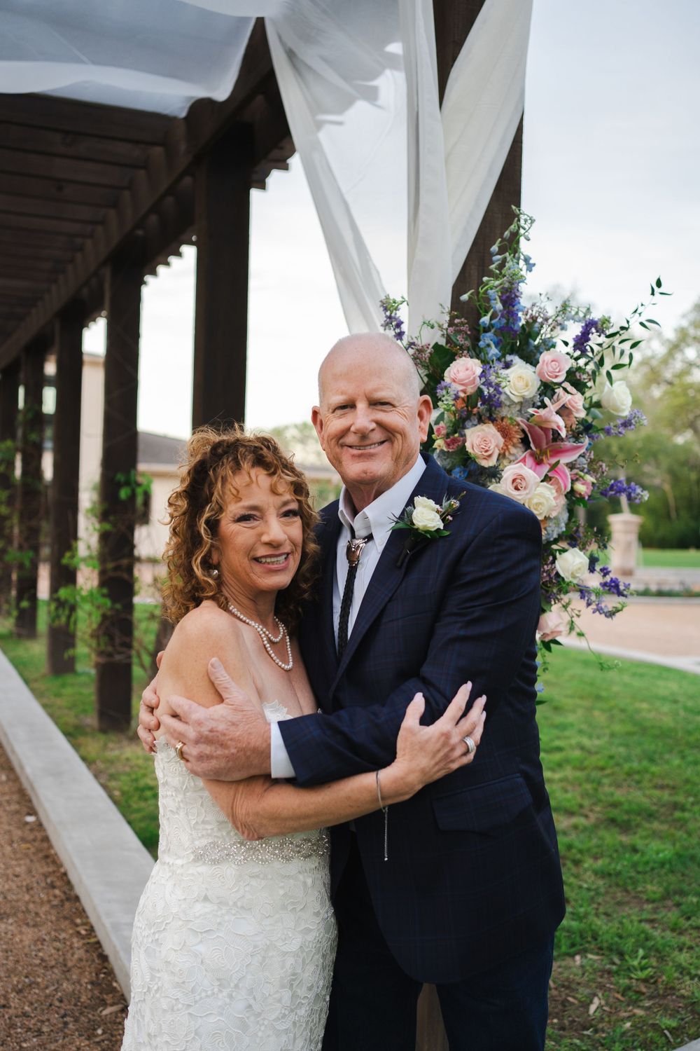 Wedding couple embracing under a covered walkway decorated with floral arrangements.