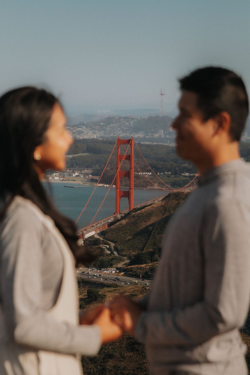 A couple stands overlooking the iconic Golden Gate Bridge and San Francisco Bay on a foggy afternoon.
