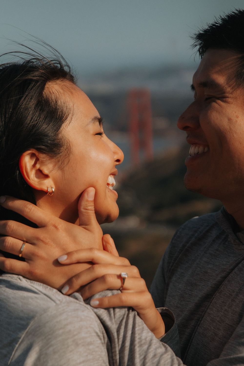 A romantic couple shares an intimate moment against a sunset backdrop with the Golden Gate Bridge visible in the distance.