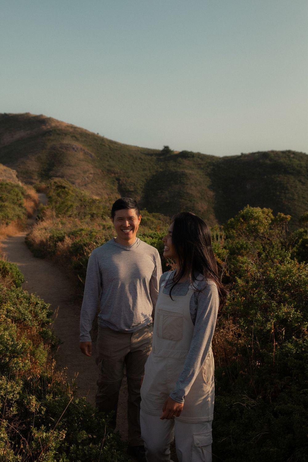 A couple enjoys an intimate moment together while walking along a scenic mountain trail at sunset.
