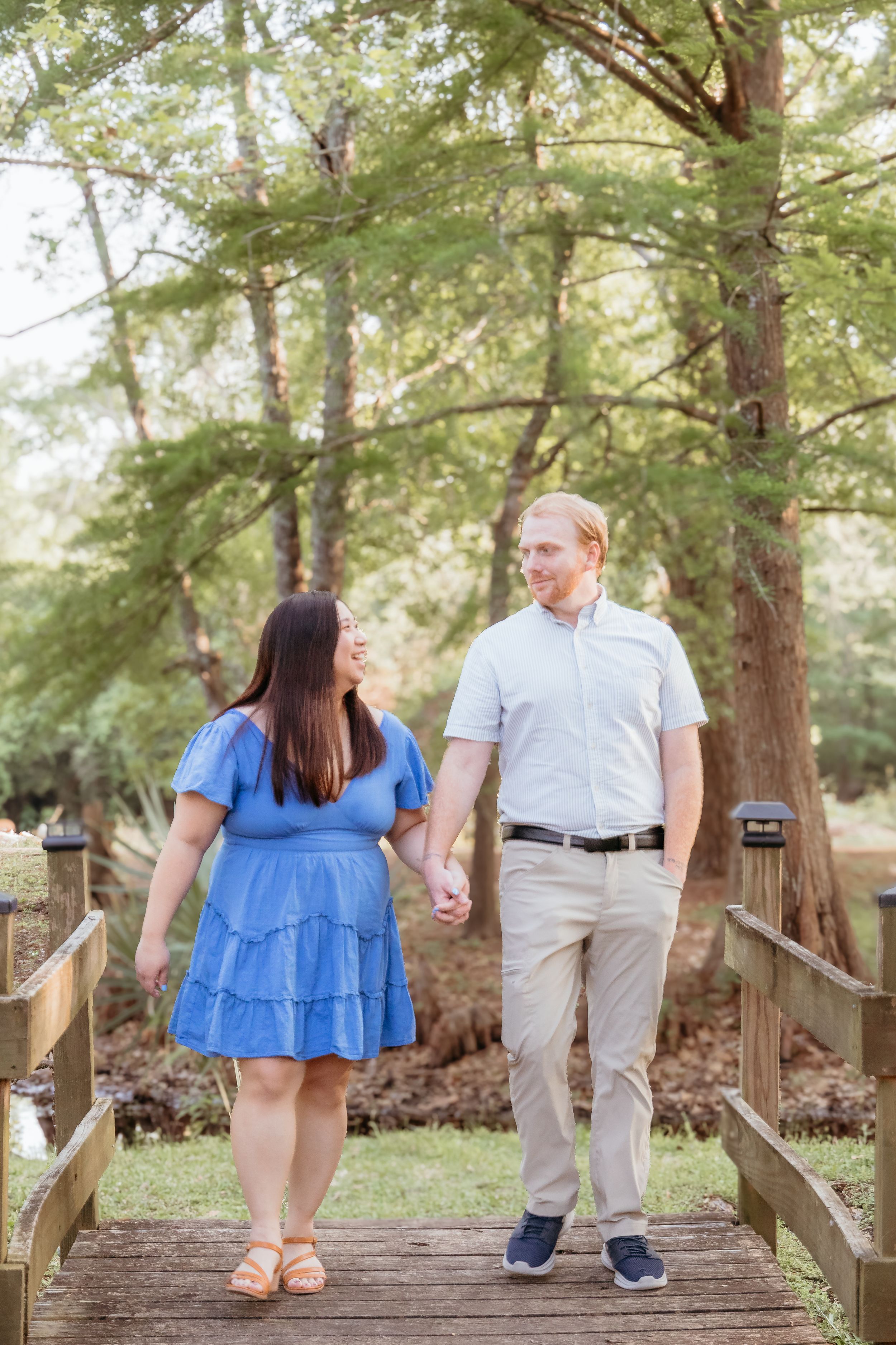 Engaged couple walking across a bridge in a forest.