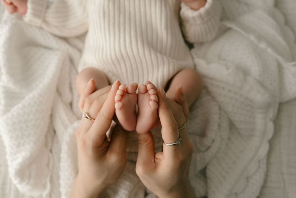 Gentle hands cradling tiny baby feet against soft white knitted fabric.