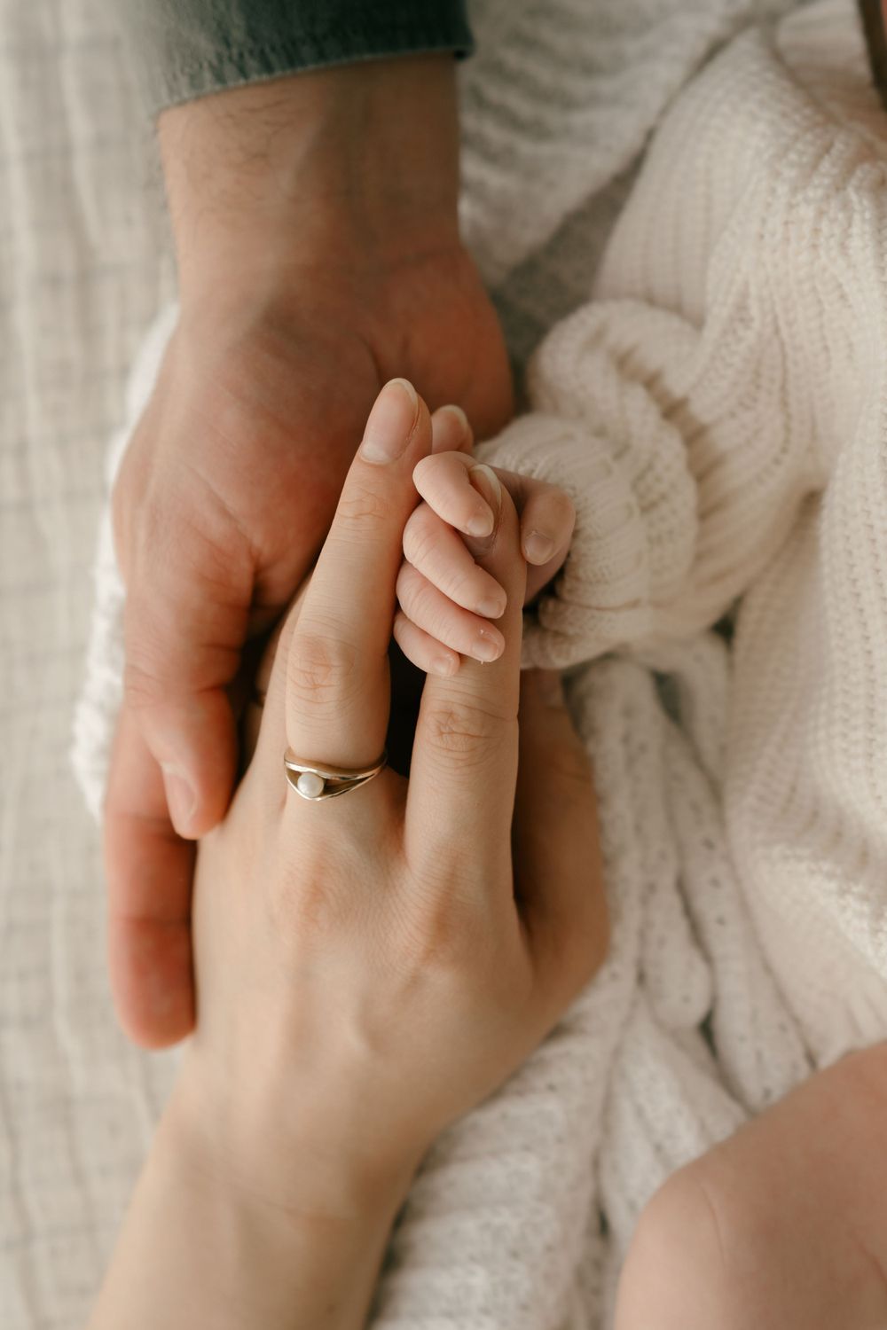 Close-up of hands holding with wedding ring and white knit fabric in tender moment.