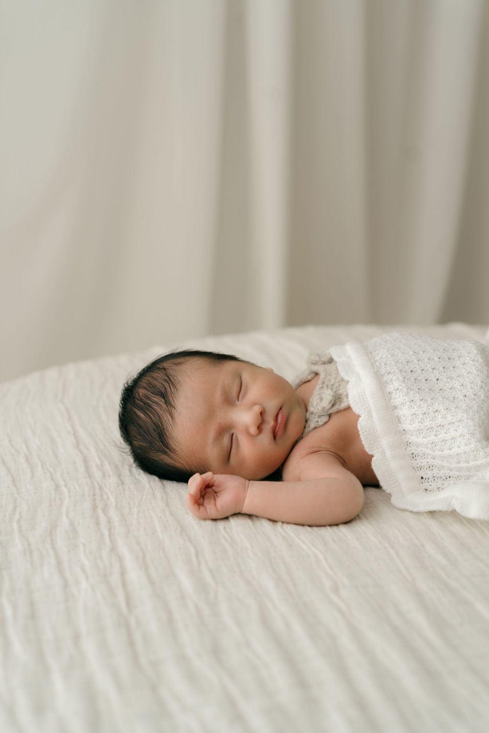 Peaceful sleeping newborn wrapped in white knitted blanket on light background.