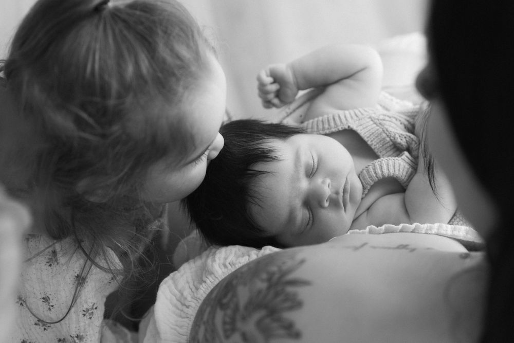 Black and white intimate portrait of parent and sleeping baby in soft lighting.