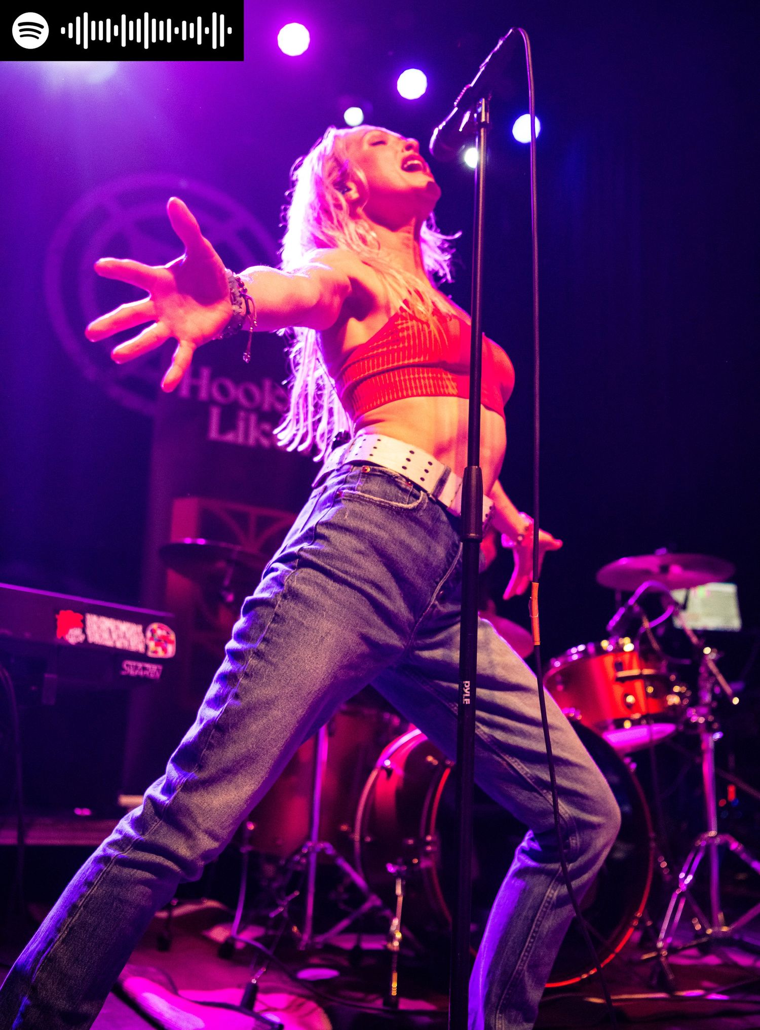Nikki singing into the mic with arms outstretched with spotify code in top left corner
