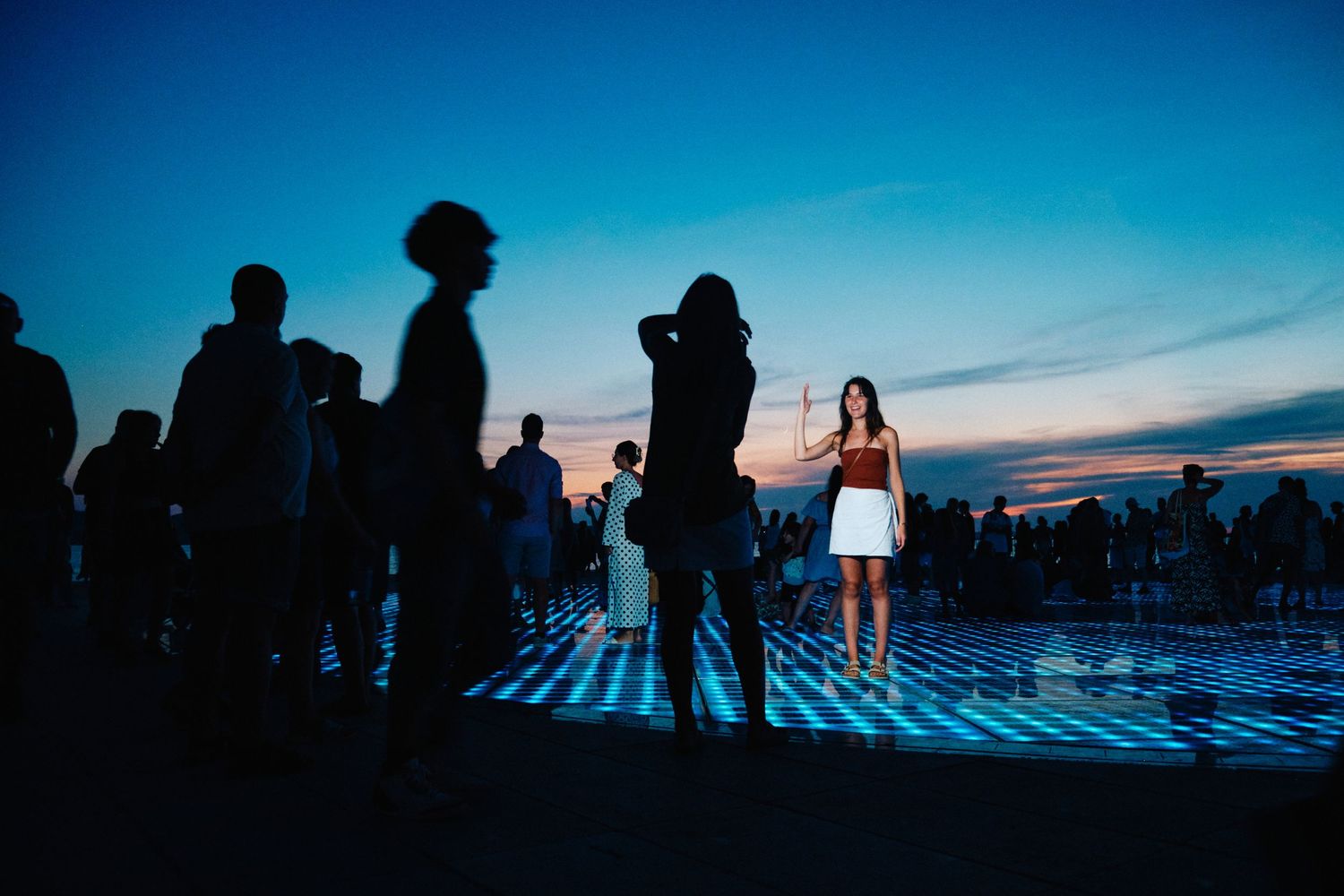 Silhouettes of people gathered at dusk on an illuminated surface with a blue sky backdrop.