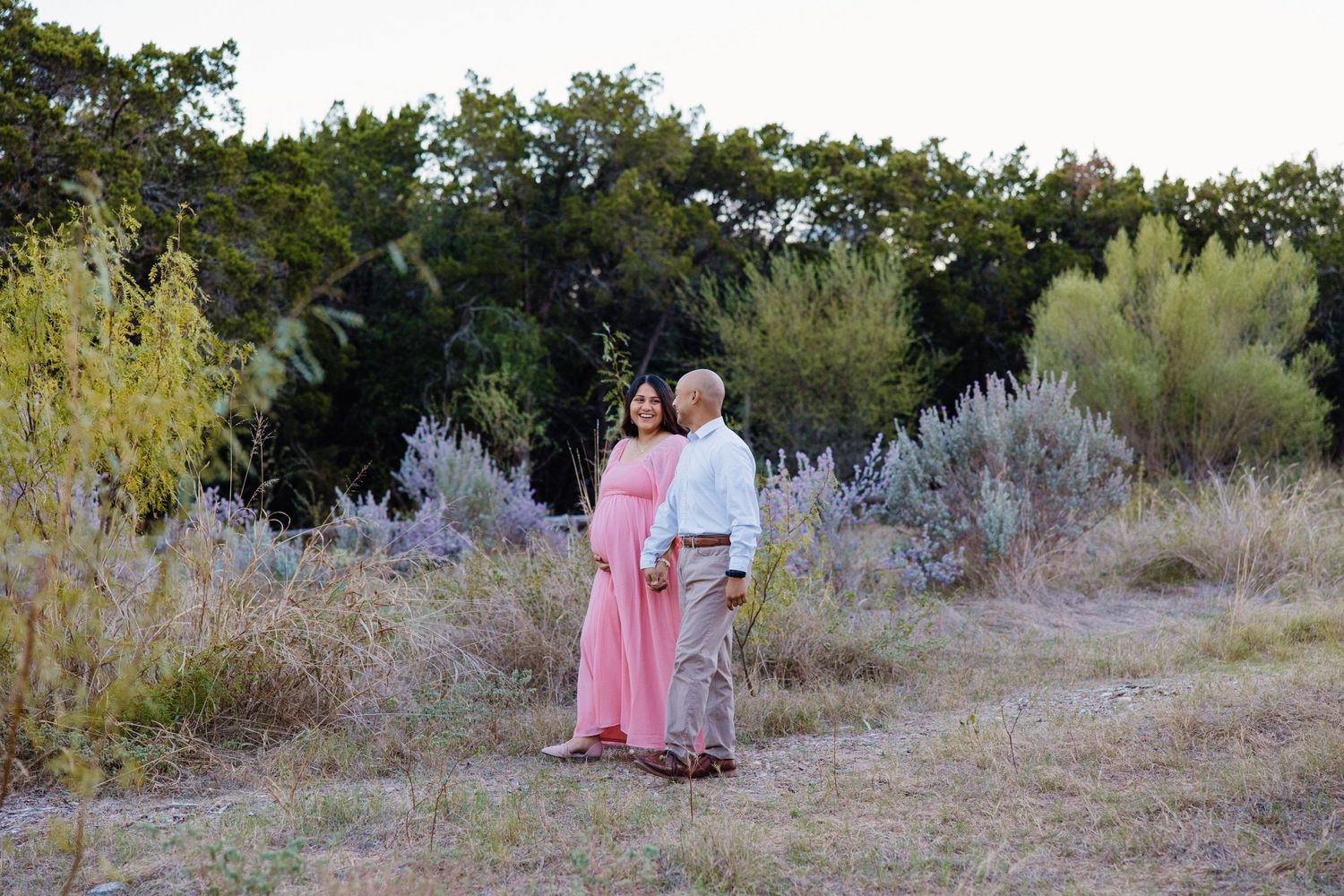 San Antonio Maternity Photography. Couple poses together in natural setting with desert brush and trees at sunset.