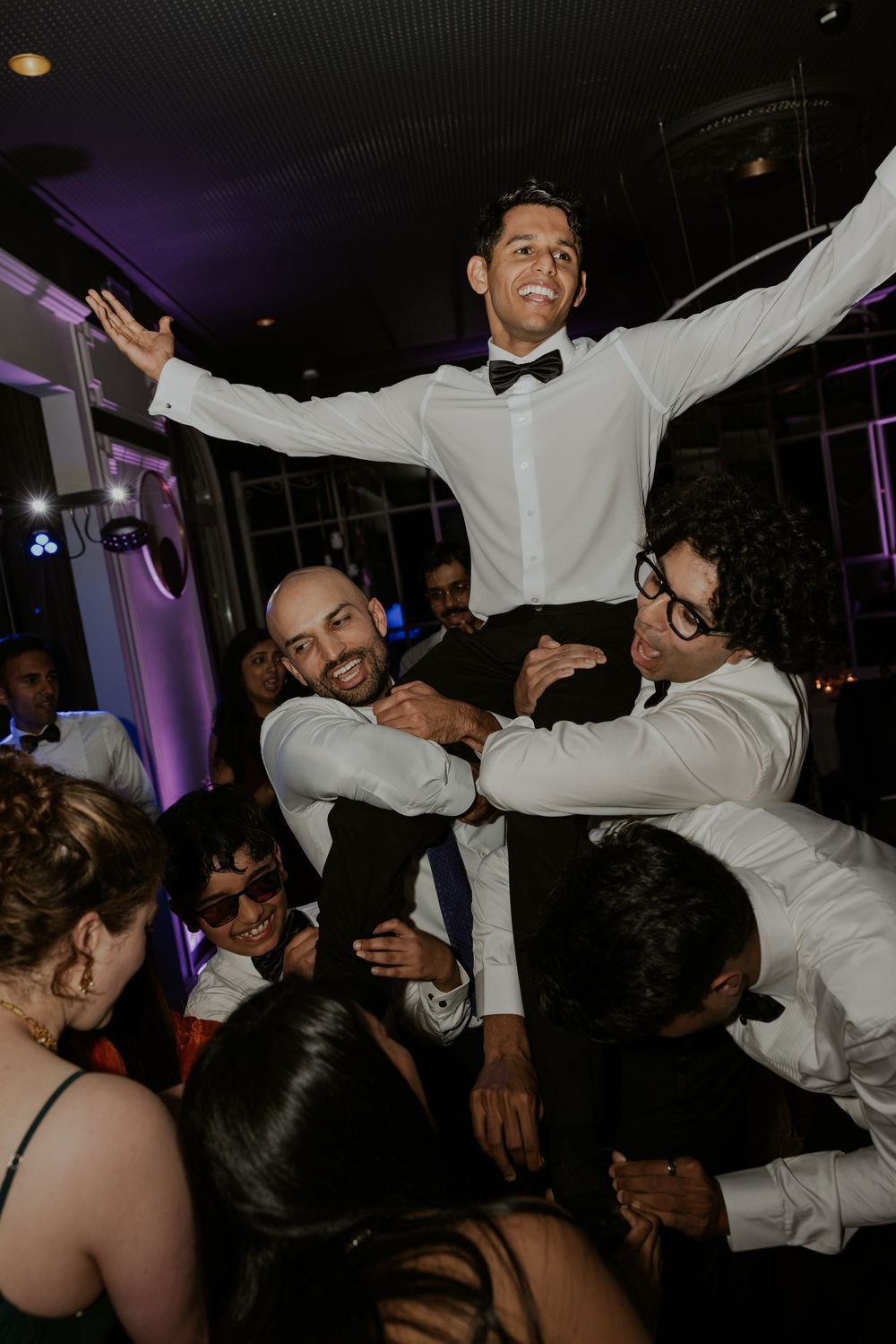 Wedding guests dancing and celebrating on a dark dance floor with purple lighting and energetic party atmosphere.