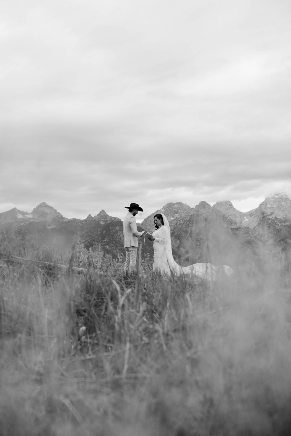 A silhouetted figure in a hat stands atop misty mountains with dramatic peaks in black and white landscape.