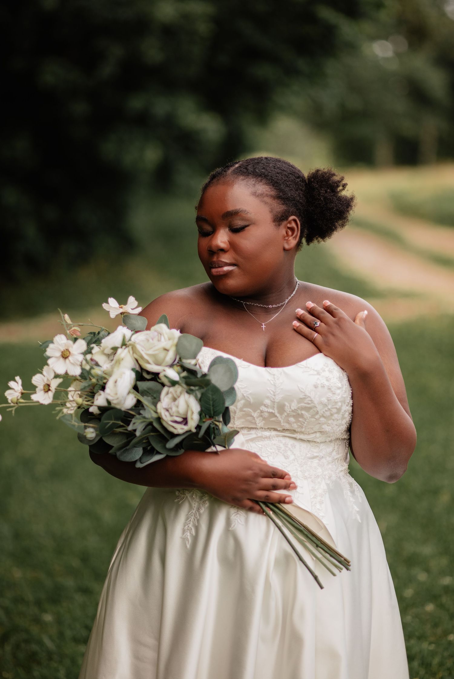 Bride in elegant white wedding dress holds bouquet of white flowers in outdoor garden setting.