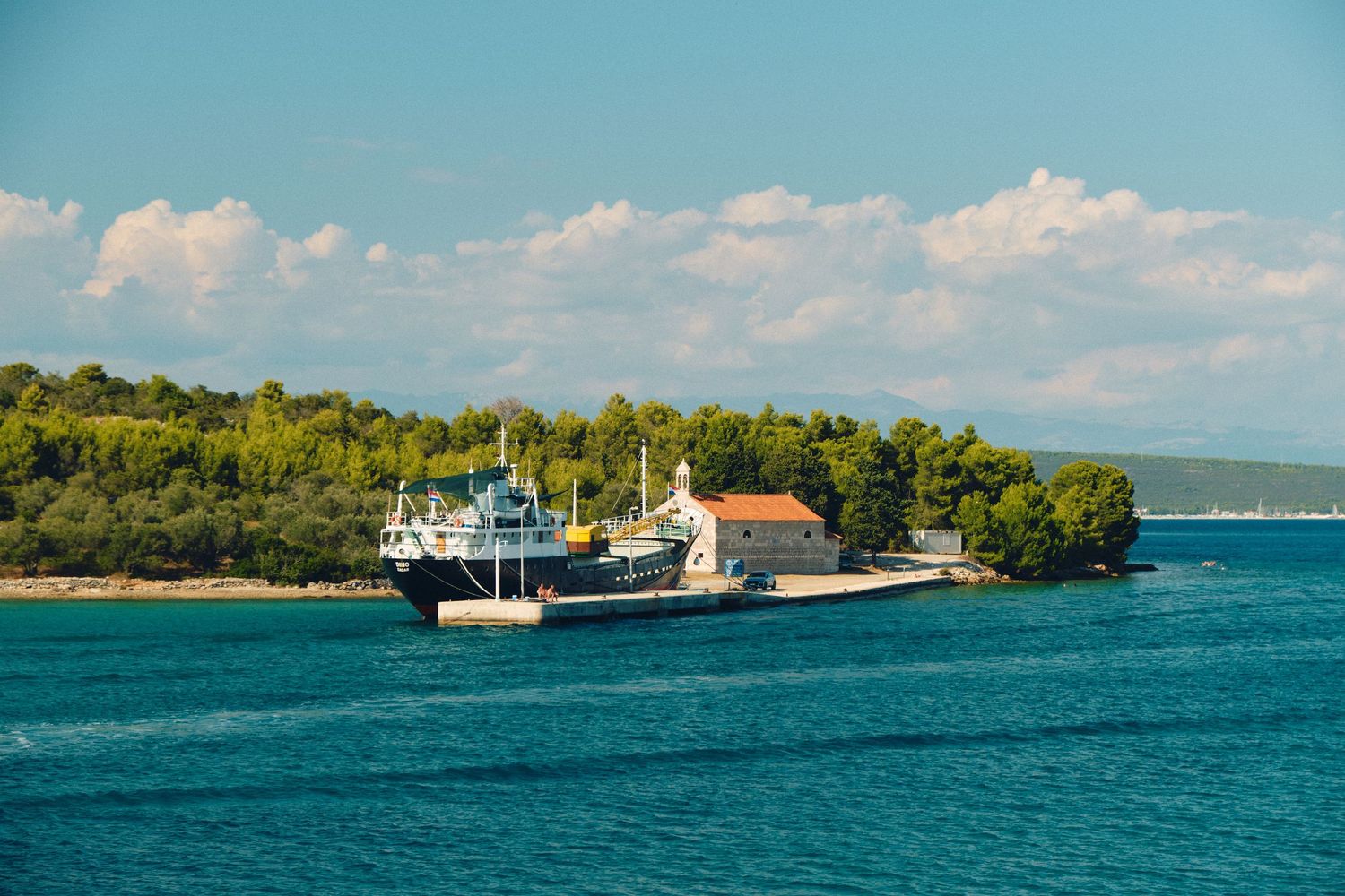 Cargo ships docked near a green island coastline in bright blue waters.