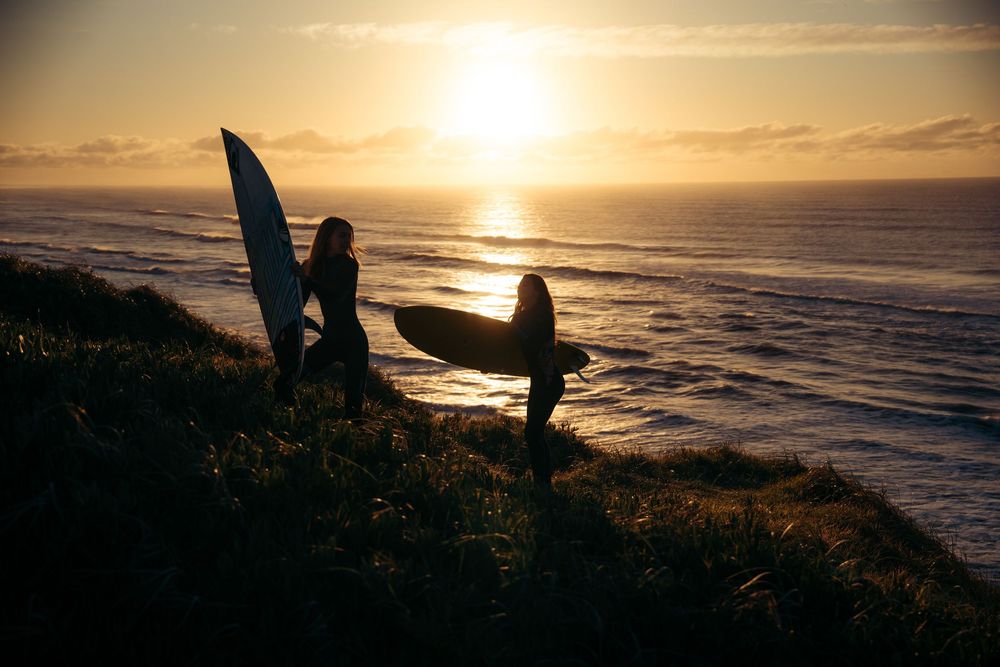 Silhouettes of surfers watching sunset over Pacific Ocean coastline.