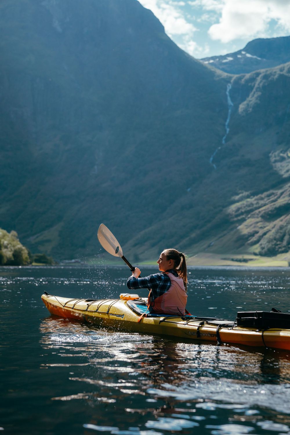 Yellow kayak gliding through scenic mountain lake waters with dramatic peaks in background.