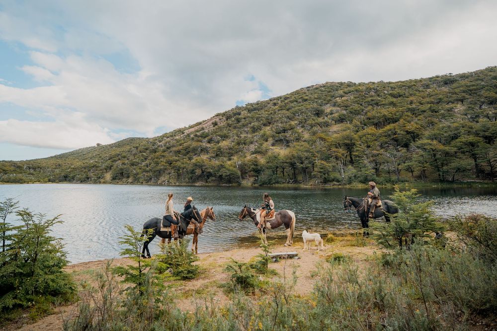 Horseback riders pause by a serene mountain lake surrounded by forested hills.