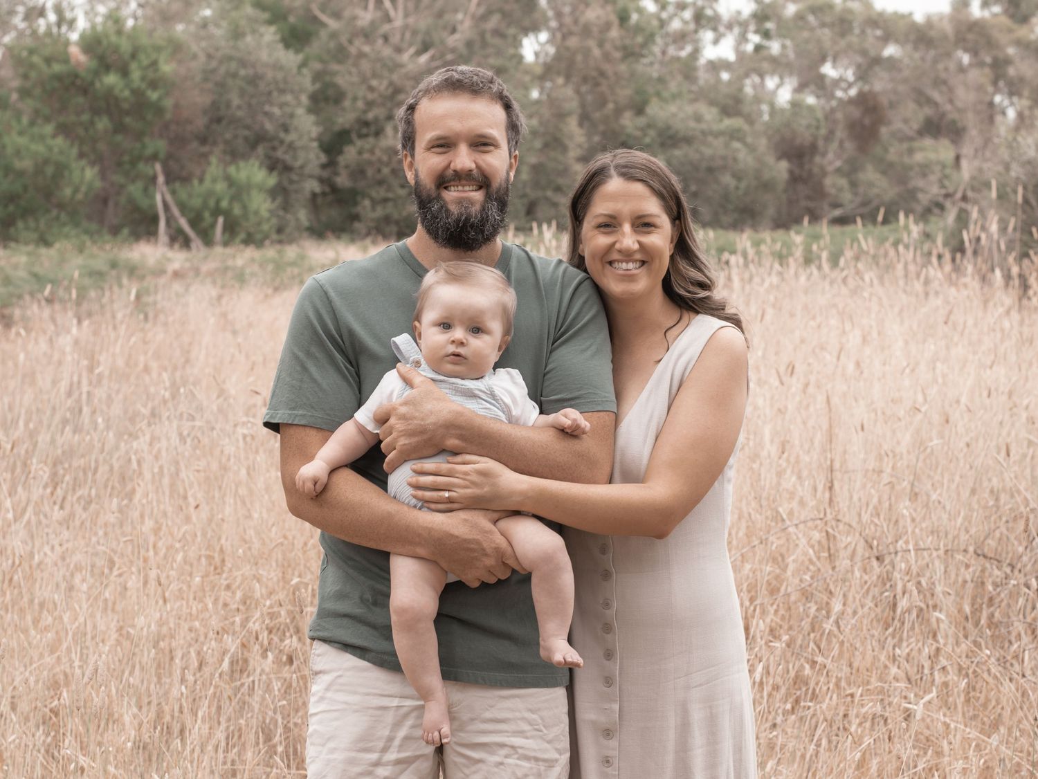 Family portrait in a rustic field with a small dog and neutral-toned clothing.