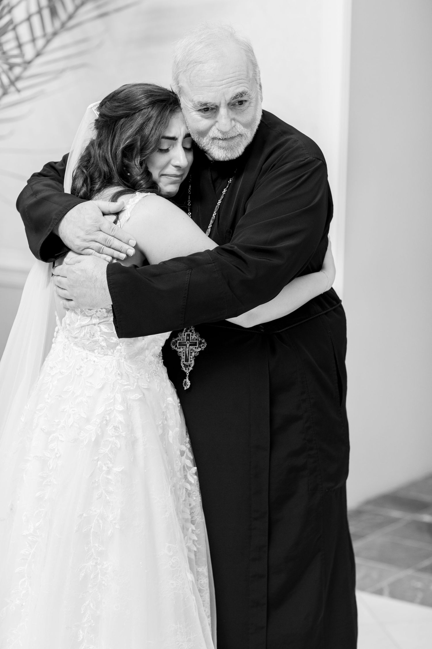 Black and white portrait of clergy member embracing bride in tender moment.