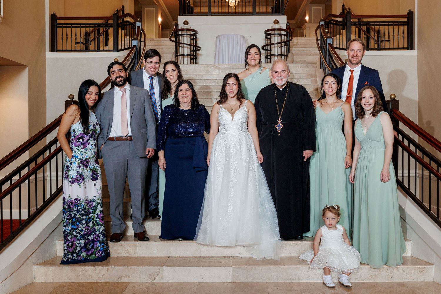 Wedding party group photo on elegant staircase with bride in white gown.