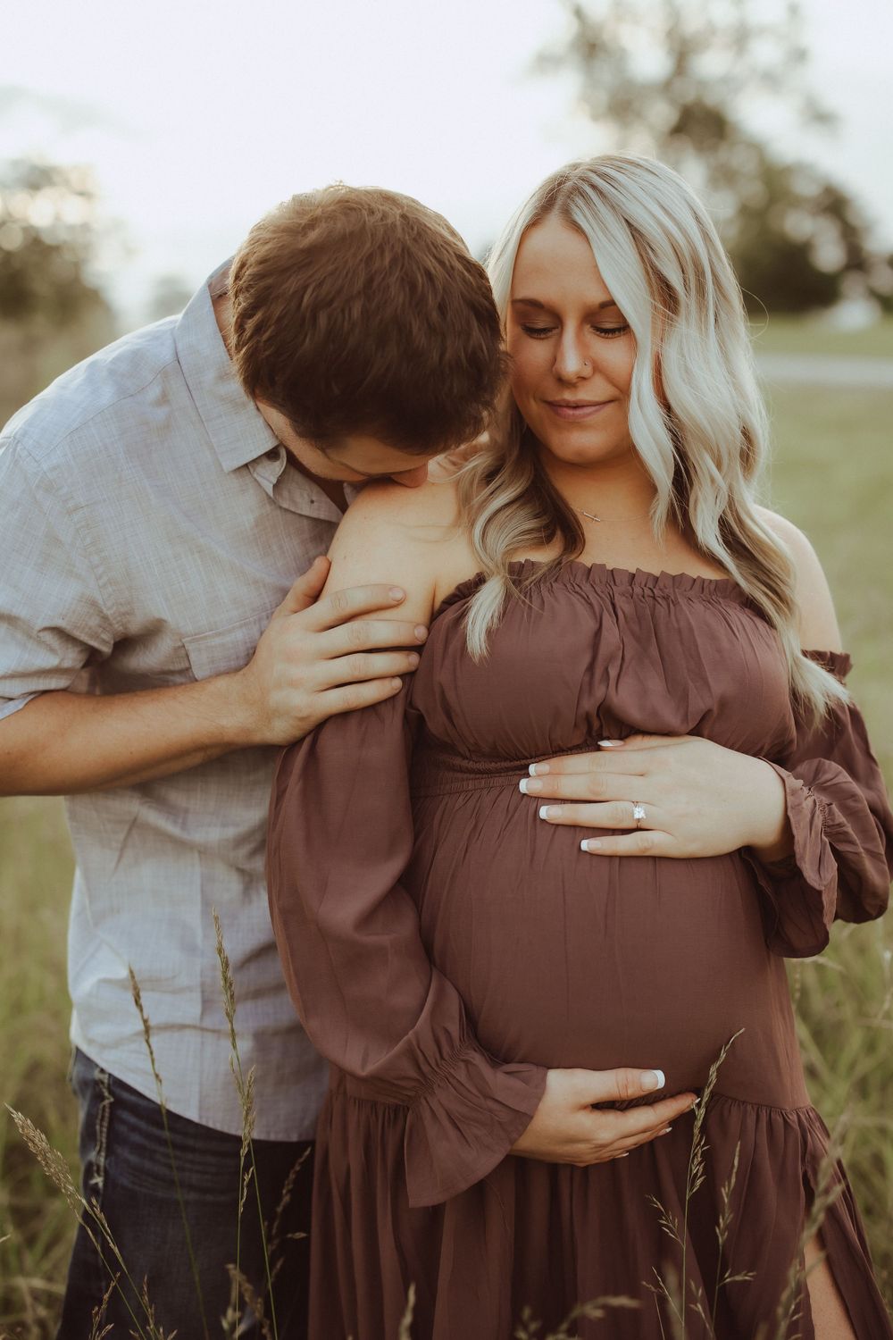 A tender embrace between a couple during an outdoor maternity photoshoot.