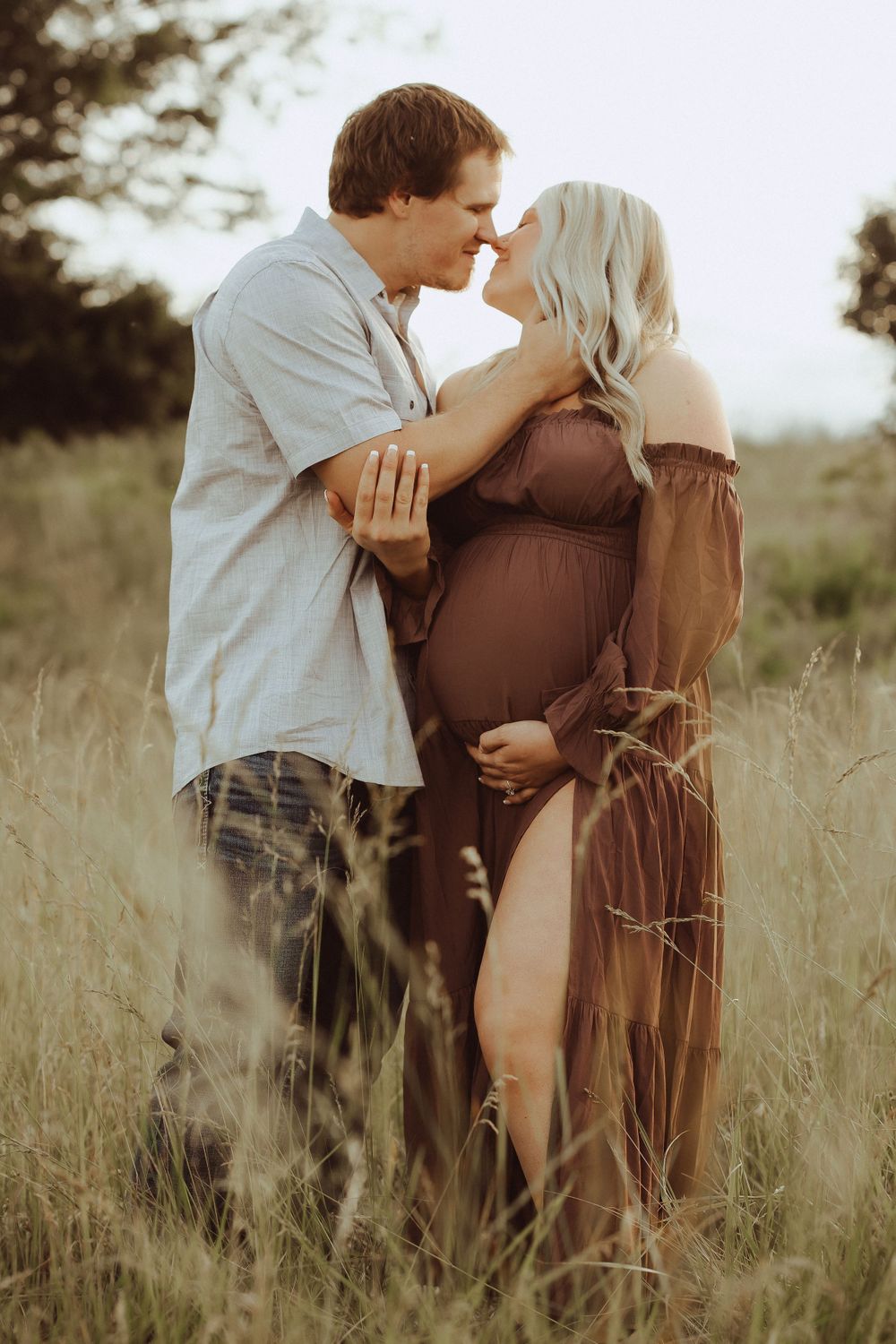 Couple embracing in tall grass field during golden hour photography session.