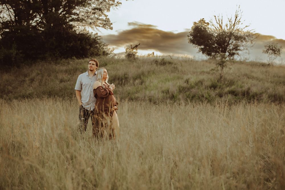 Scenic outdoor maternity photoshoot in a natural grassland setting.