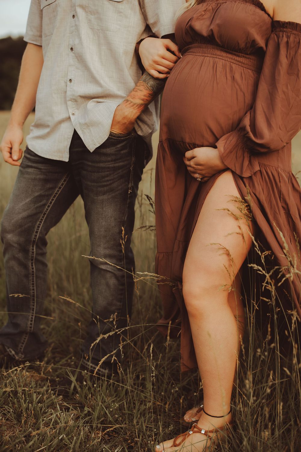 A couple embraces in a field of tall grass during a romantic maternity photoshoot at sunset.