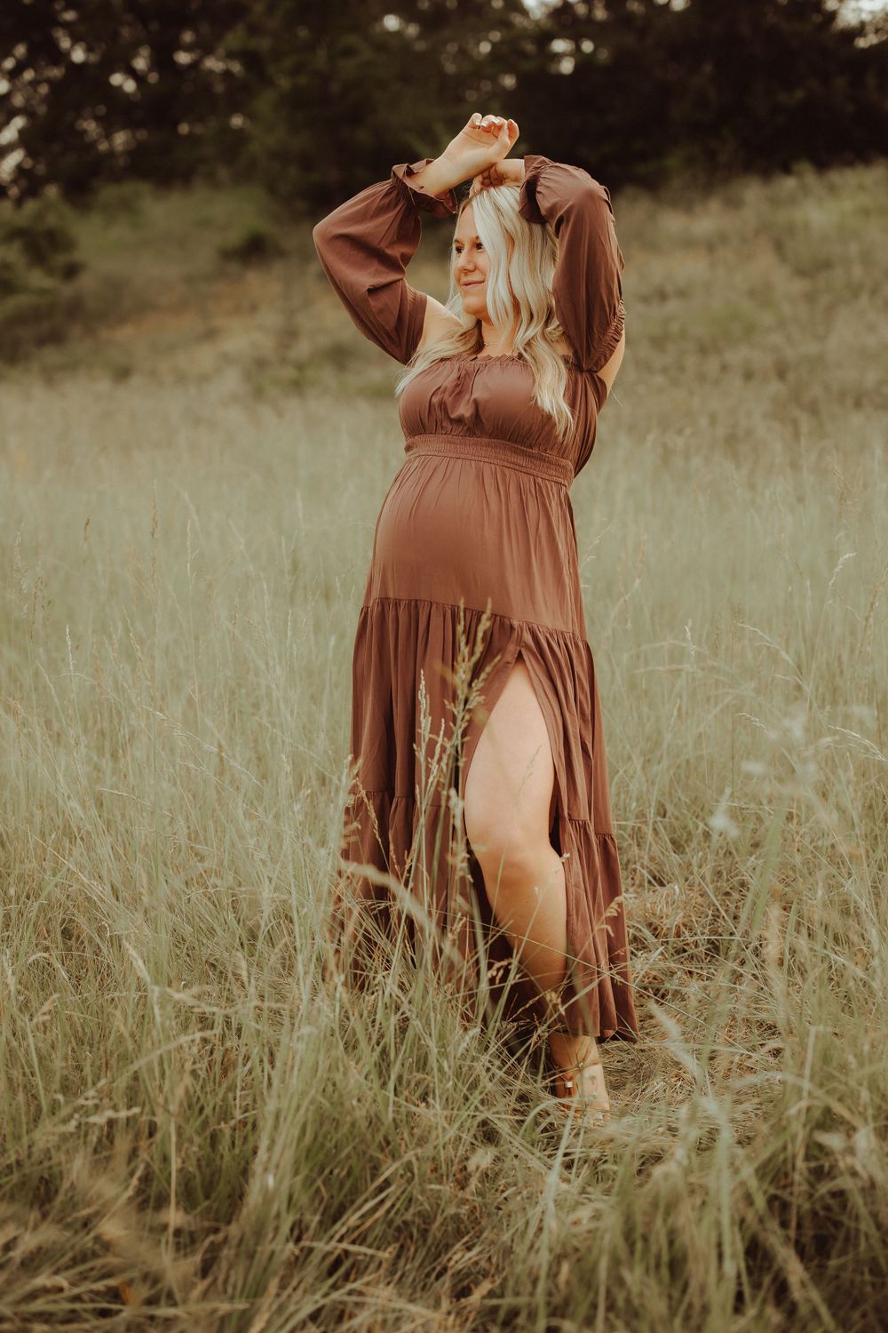 A person in a flowing brown dress poses gracefully in a field of tall grass.