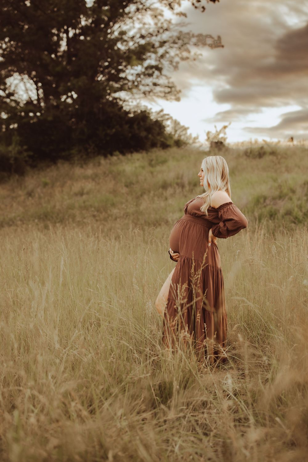 A person in a brown dress walks through a sunlit meadow with tall grass.