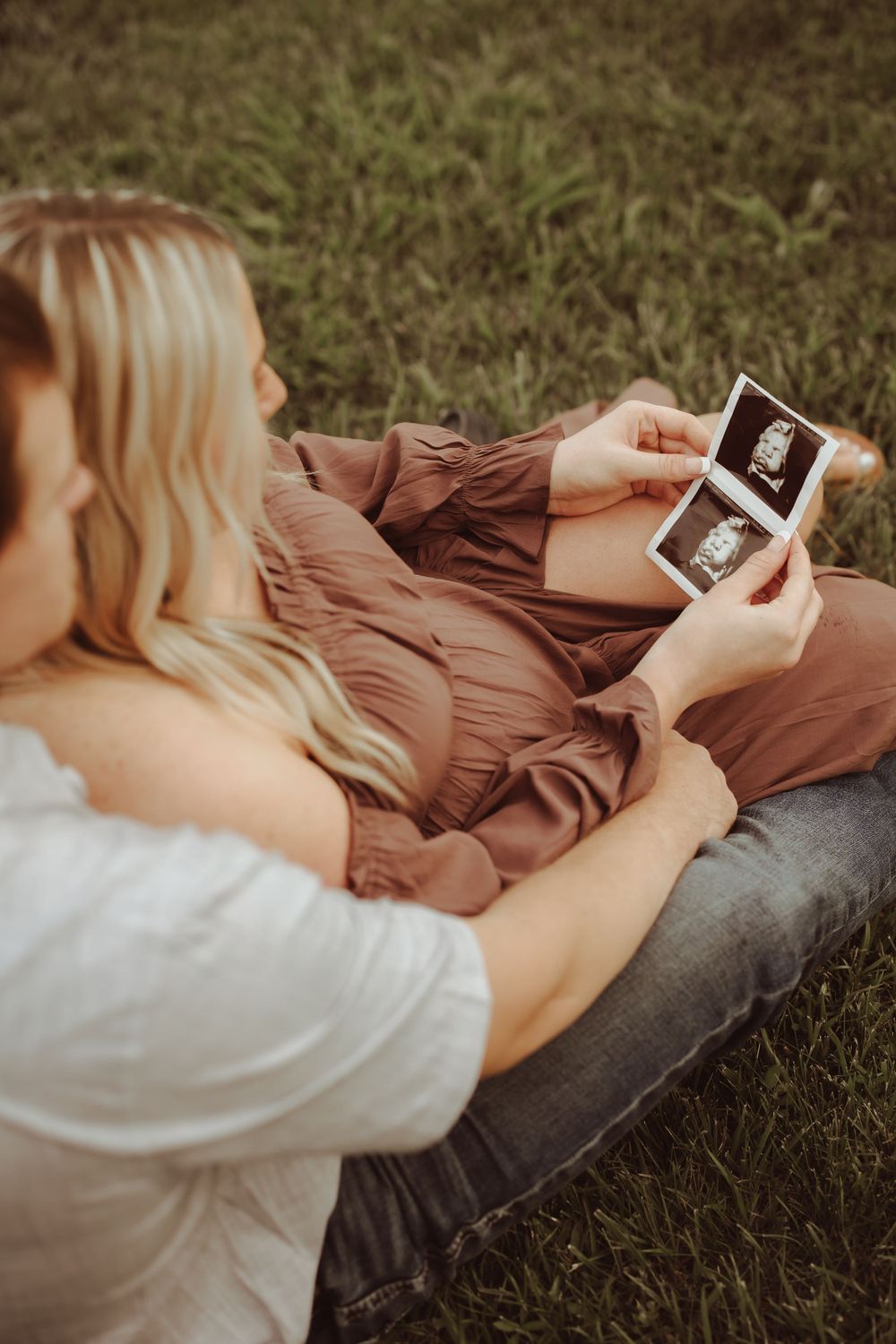Someone lying on grass holds up an ultrasound photo during a pregnancy announcement photoshoot.