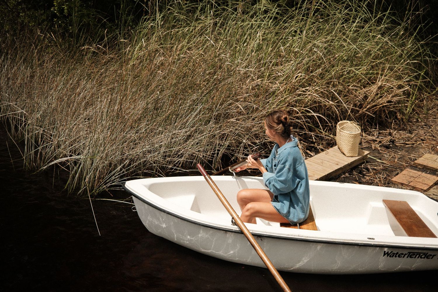 Small white rowboat floating in calm water surrounded by tall grass.