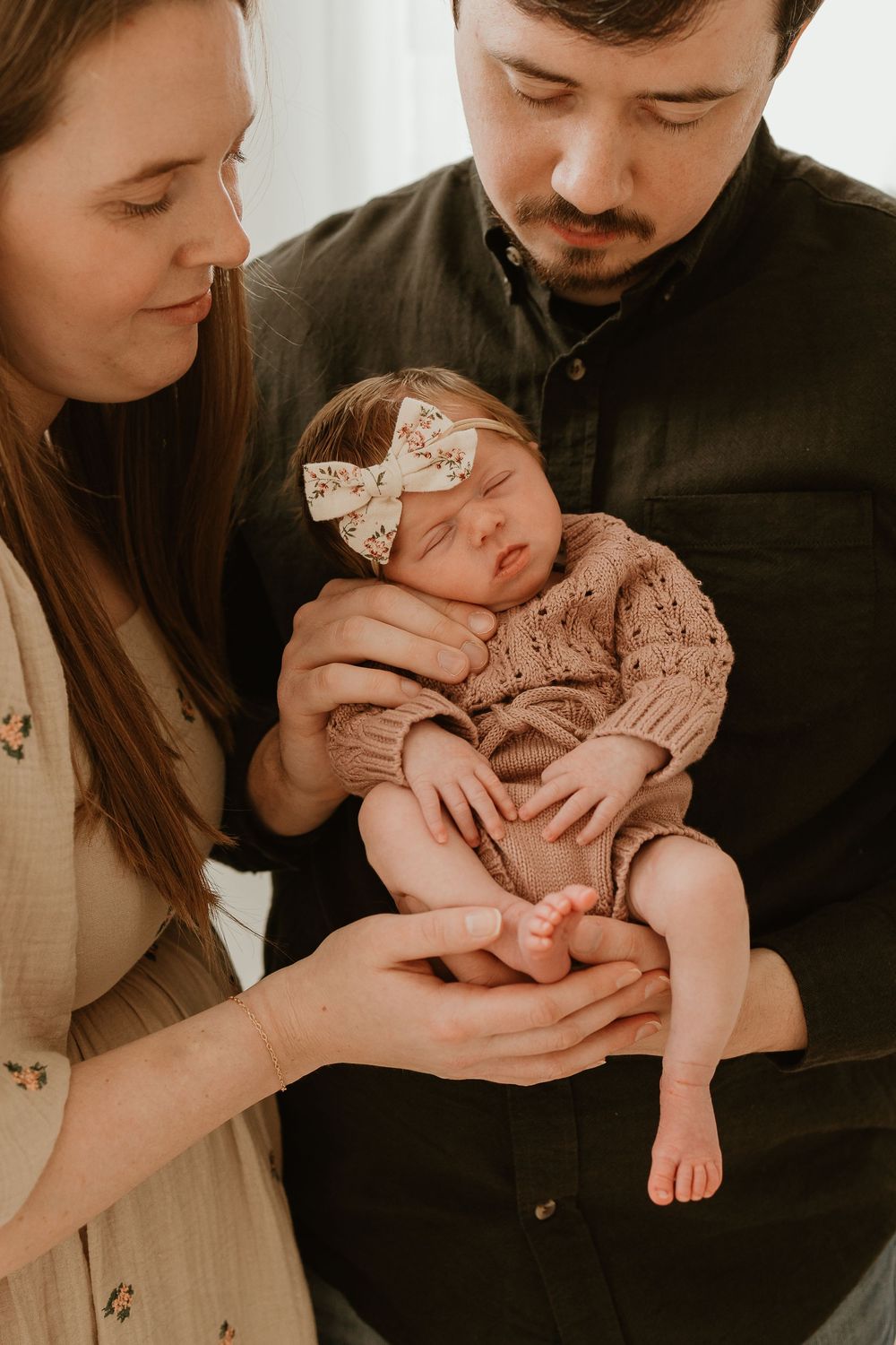 A couple holds and kisses their newborn baby in a series of tender black and white photographs.