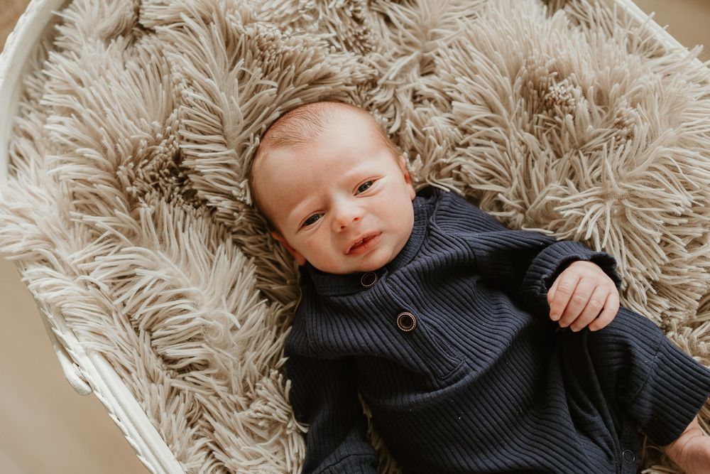 A baby wearing a dark knit sweater lies on a plush beige shag rug.