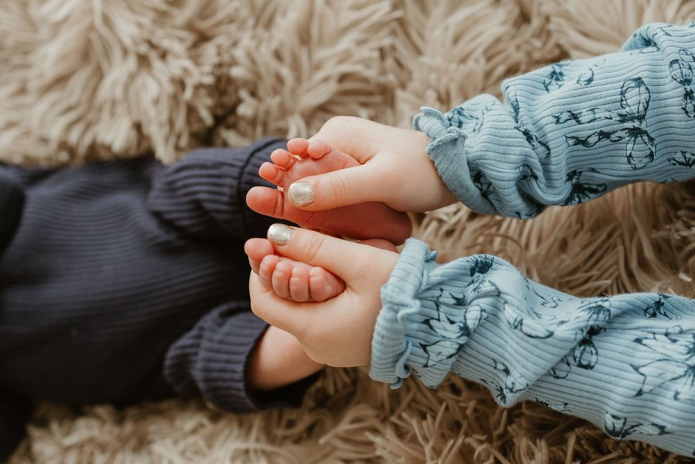 A close-up view of hands holding a newborn baby's tiny foot in soft blue clothing.