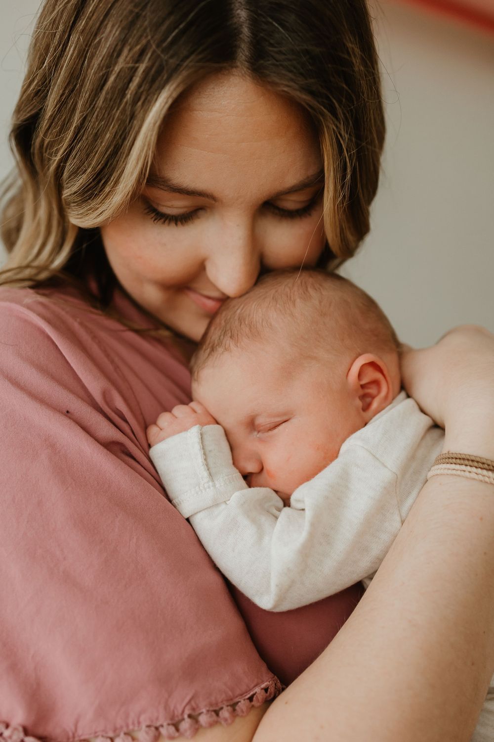 A tender moment between mother and baby in soft pink tones as they share an intimate embrace.