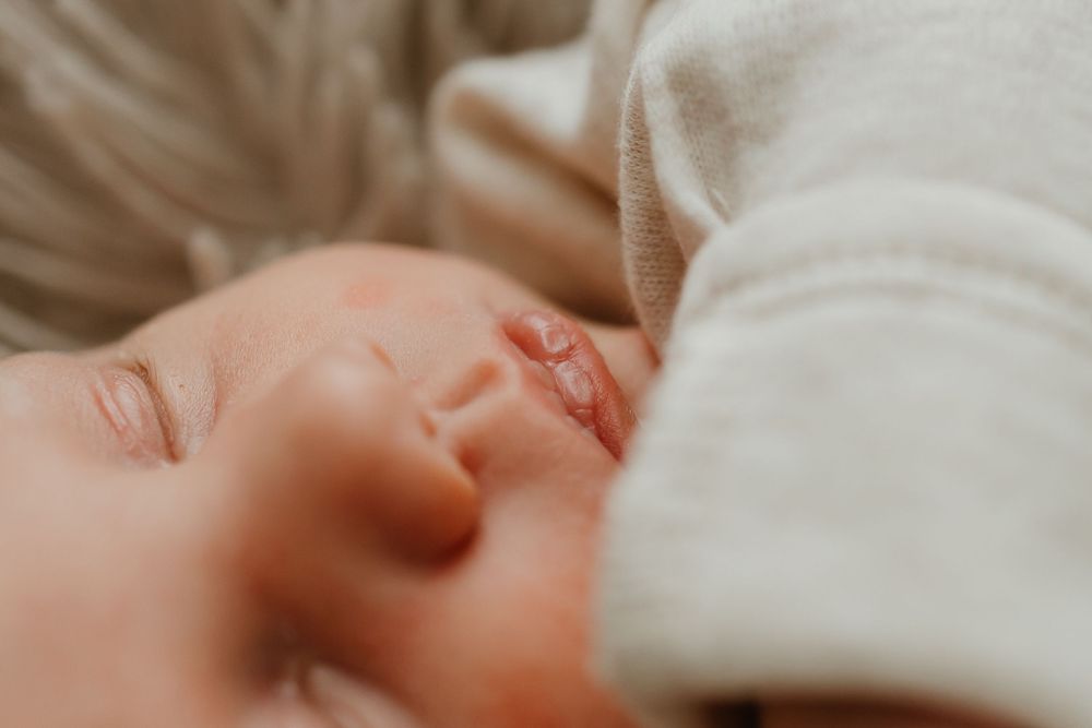 A sleeping baby in soft white clothing rests peacefully in a close-up shot.