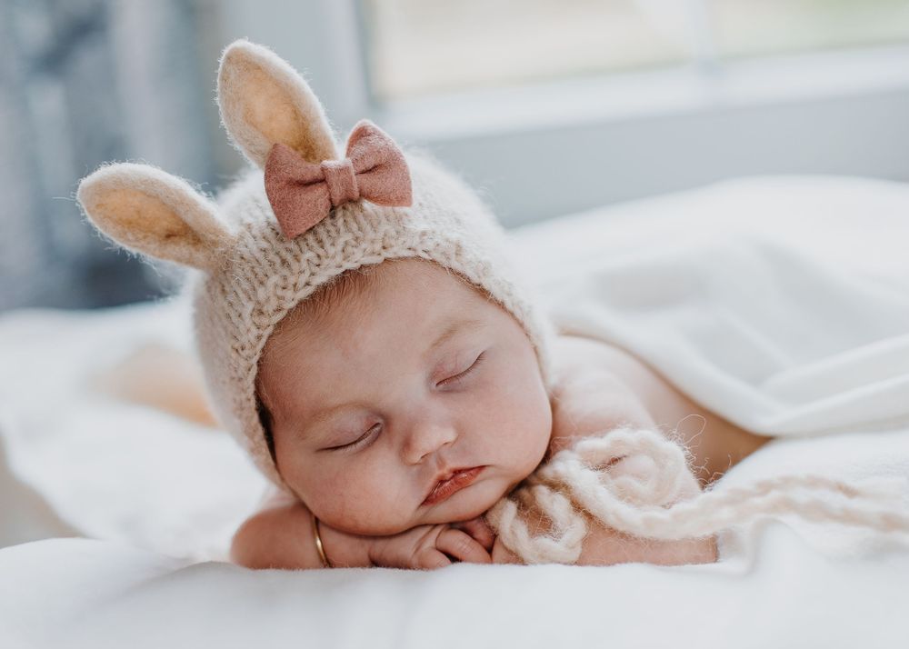 Newborn baby posed on hands in easter hat with bunny ears.