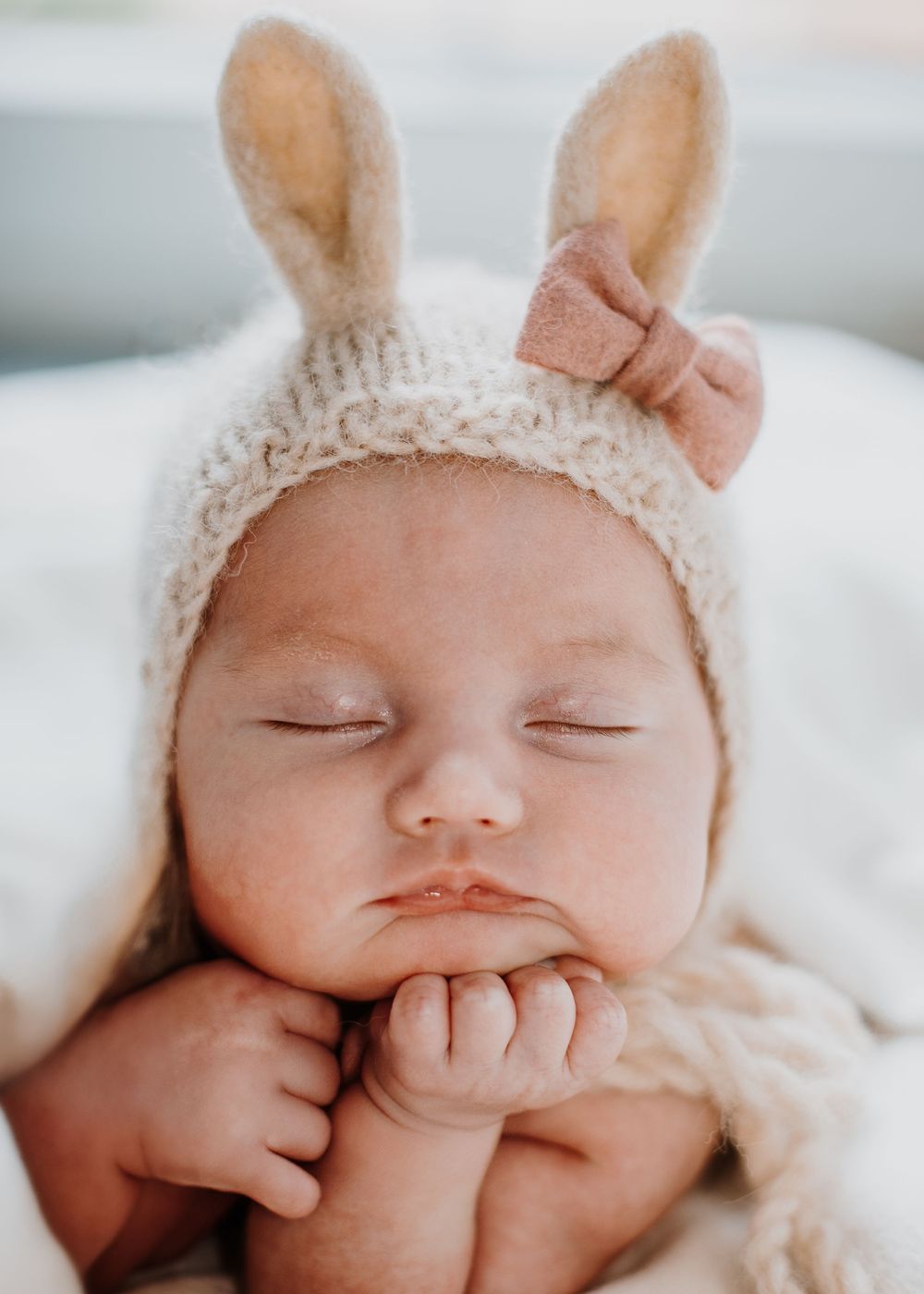 Newborn baby posed on hands in easter hat with bunny ears.