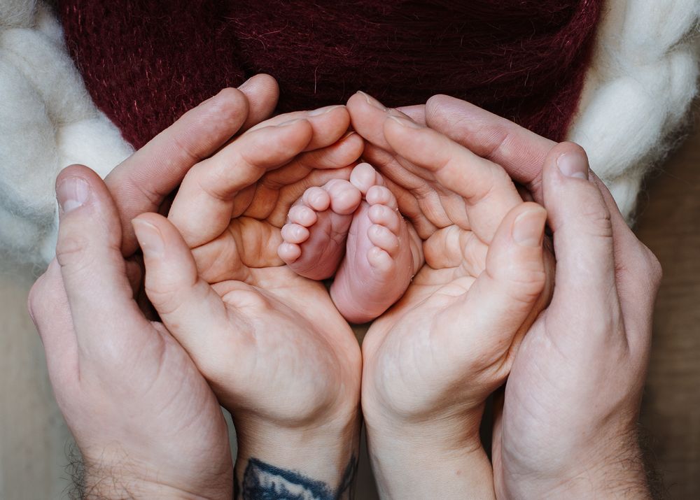 Close Detail shot of parent's hands holding newborn baby's feet.