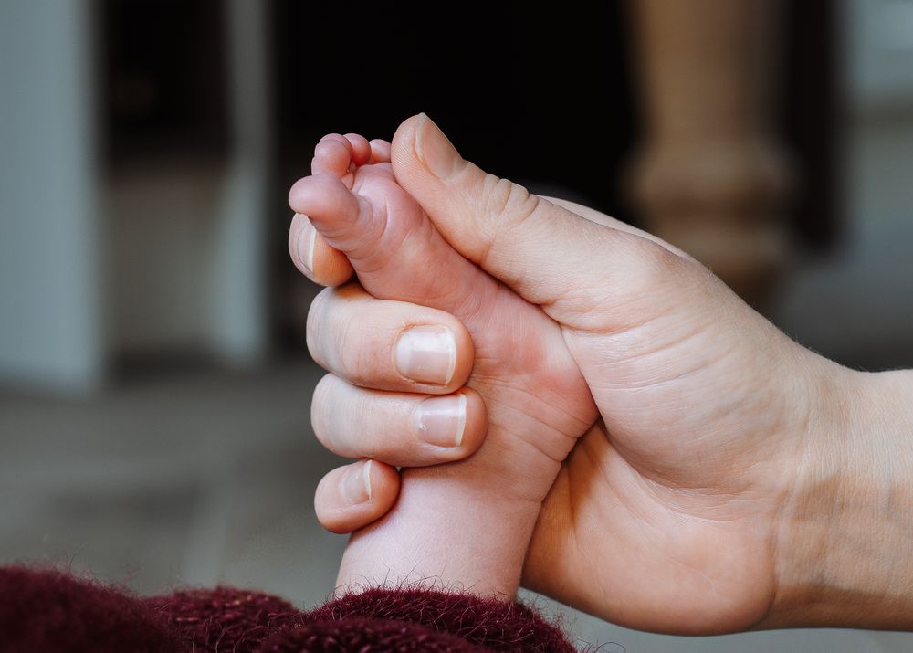Close Detail shot of parent's hands holding newborn baby's foot.