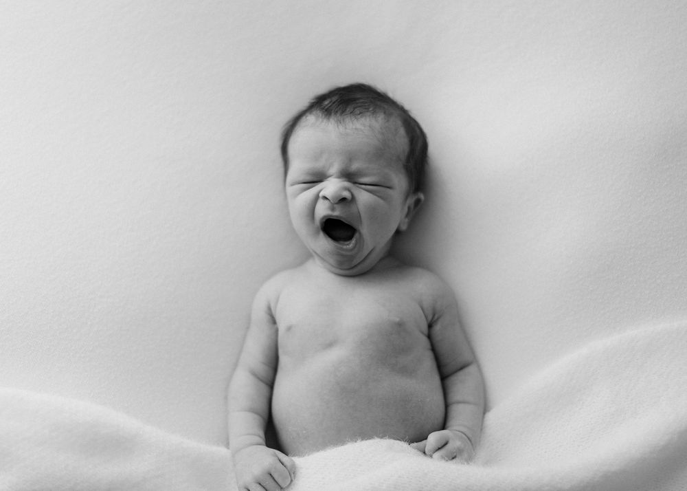 Black and white image of a crying newborn baby wrapped in a soft blanket on a light background.