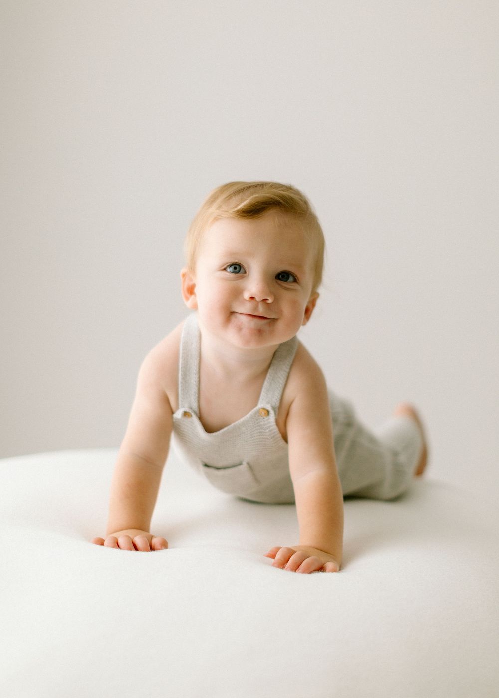 A baby in a white tank top crawls and smiles on a white background in a progression of three poses.
