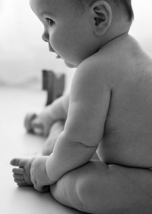 Black and white artistic photograph of a chubby baby in profile sitting and leaning forward.