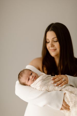 A sleeping newborn baby wrapped in a white knit blanket rests peacefully in loving arms.