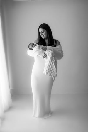 Black and white sequence of photos showing gentle interaction between mother and baby in minimalist studio setting.